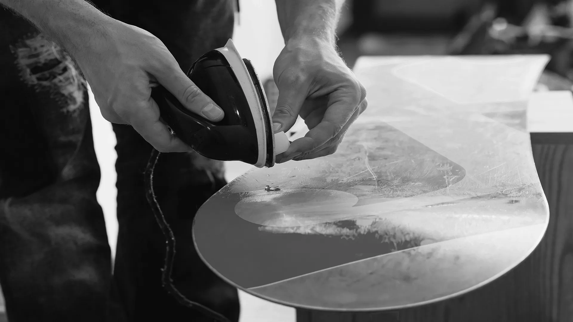 スノーボードにアイロンでホットワックスをかけている様子の写真