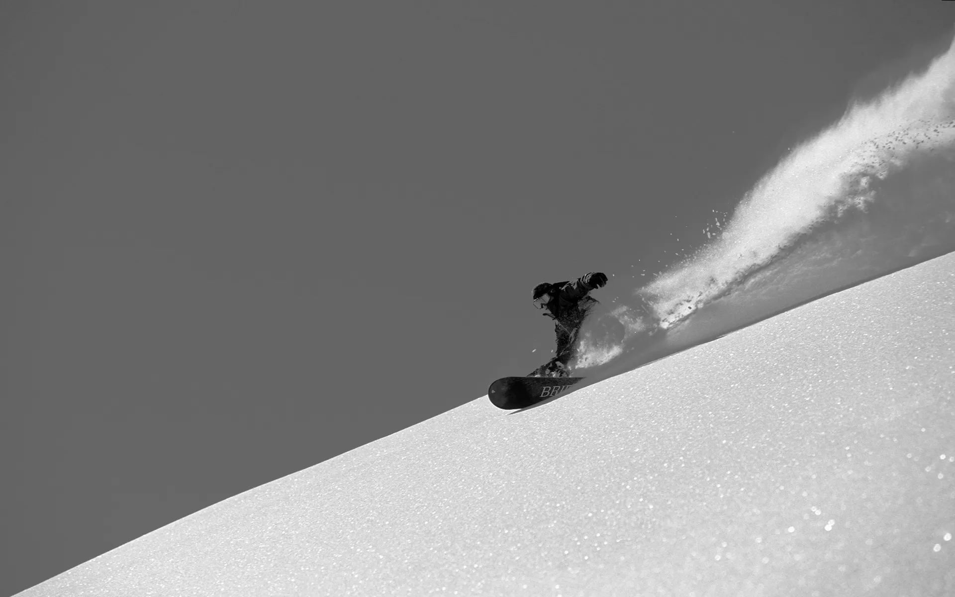 JPが真っ白な雪の上をスプレーを上げながらスノーボードで滑っている写真